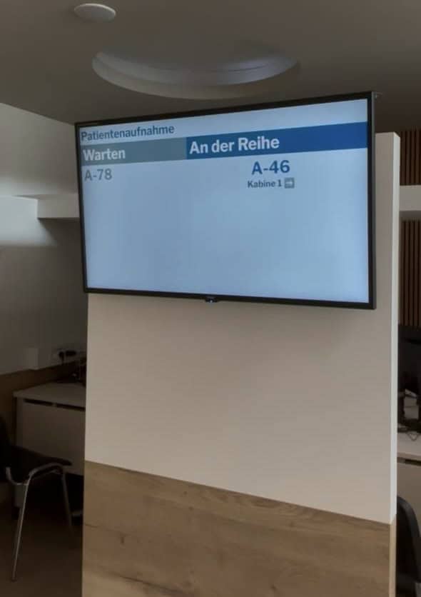 Aufrufmonitor in der Patientenaufnahme einer Klinik zeigt wartende und aufgerufene Wartenummern mit Kabine